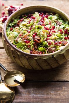 a wooden bowl filled with lettuce and cranberries next to two spoons