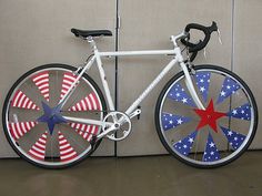 a white bicycle with red, white and blue spokes is parked in front of a wall