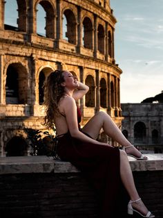 a beautiful woman sitting on top of a brick wall next to an old building in the background