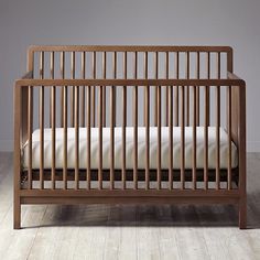 a wooden crib with white sheets on the floor in front of a gray wall