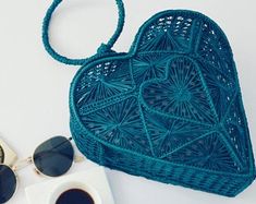 a blue heart shaped purse next to a cup of coffee and sunglasses on a white surface