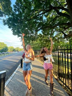 two girls are walking down the sidewalk with their arms in the air