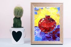 a painting next to a potted cactus on a white table with a black heart