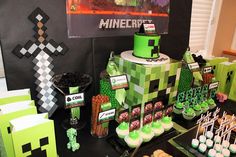 a table topped with cake and cupcakes covered in green frosting next to minecraft decorations