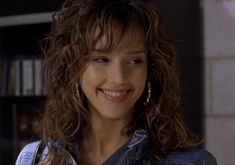 a close up of a person wearing a jean jacket and smiling at the camera with bookshelves in the background