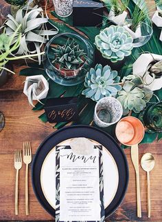 a table setting with black and white plates, silverware and succulents