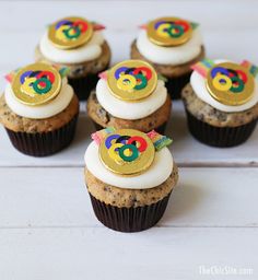 some cupcakes with white frosting and gold decorations on top are sitting on a table