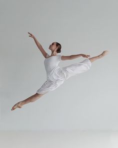 a woman is jumping in the air with her arms outstretched and legs spread wide, wearing white clothing