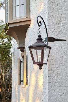 an outdoor wall light on the side of a white building with palm trees in the background