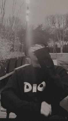 a man sitting on top of a wooden bench wearing a sweatshirt with the word dio printed on it