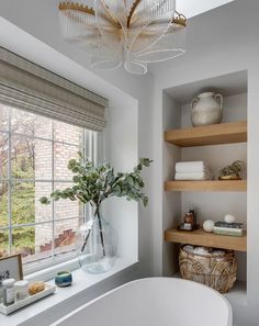 a white bath tub sitting under a window next to a shelf filled with towels and other items