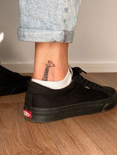 a giraffe tattoo on the ankle of a woman's foot, next to a pair of jeans