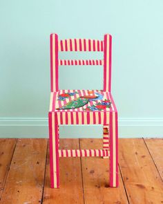 a pink and red chair sitting on top of a wooden floor next to a blue wall