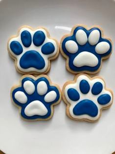 four decorated cookies with blue and white icing in the shape of paw prints on a plate