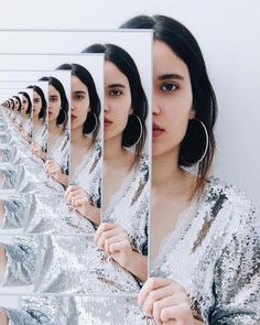 a woman holding up a mirror to show her reflection in front of the mirror, with multiple identical images behind it