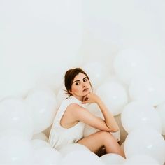 a woman sitting in the middle of white balloons