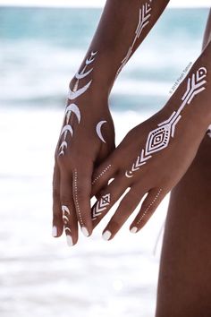 two women with white tattoos on their arms and hands near the water's edge