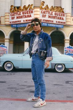 a man standing in front of a car talking on a cell phone while wearing sunglasses