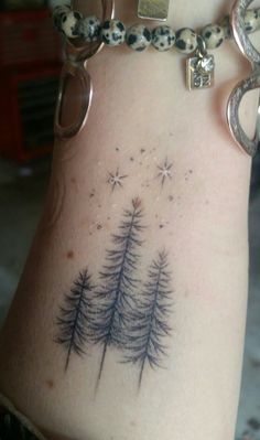 a woman's arm with a pine tree tattoo on the back of her stomach