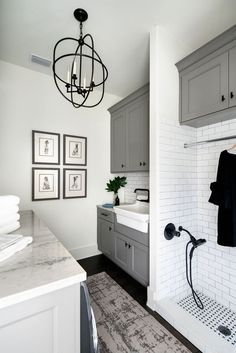 a white bathroom with gray cabinets and marble counter tops on the sink, shower head, and rug