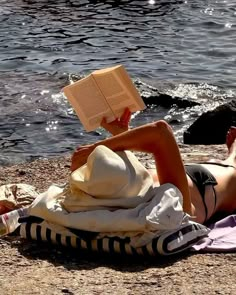 a woman reading a book while laying on the ground by the water's edge