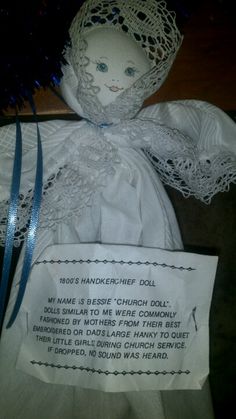 a white cloth doll with a blue ribbon around it's neck and handwritten label