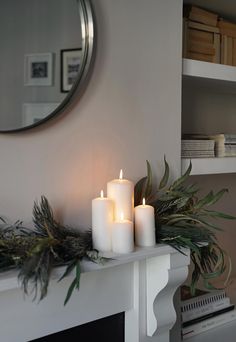 three lit candles sit on a mantle in front of a mirror