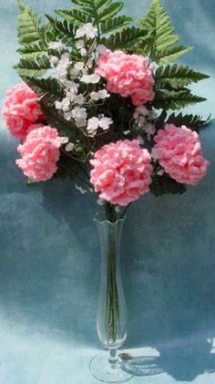 a vase filled with pink flowers on top of a blue table covered in green leaves