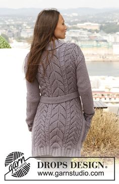 a woman standing in front of a lake wearing a gray sweater dress