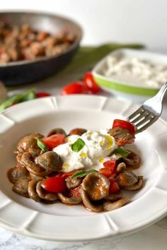 a white plate topped with mushrooms covered in fettuccine, tomatoes and sour cream