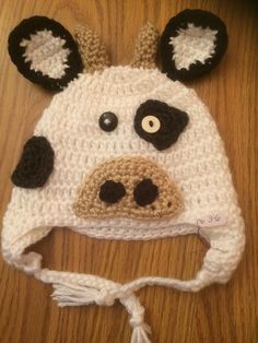 a crocheted cow hat with ears and eyes on top of a wooden table