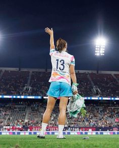 a female soccer player is standing on the field with her hand up in the air