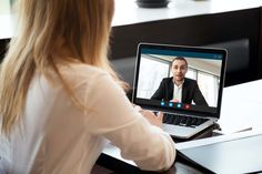 a woman sitting in front of a laptop computer with a video call on the screen