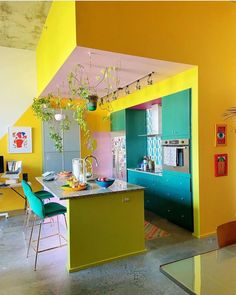 the kitchen is painted bright yellow and has blue chairs, green counter tops, and an island