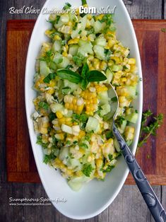 a white bowl filled with corn and cucumber on top of a wooden table