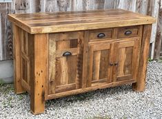 an old wooden cabinet sitting on gravel next to a wall with wood planks and metal knobs