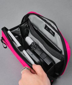 a person is opening the back compartment of a pink bag with pens and pencils in it