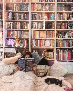 a woman sitting on a couch reading a book in front of a bookshelf full of books