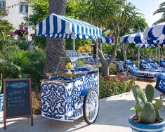 an ice cream cart with blue and white striped awnings next to palm trees