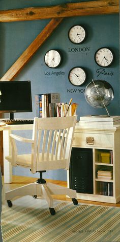 there are many clocks on the wall behind this desk and chair in front of it