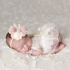 a baby is laying down wearing a white dress and a pink flower in her hair