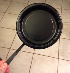 a person holding a black paper plate on top of a tiled floor next to a wall