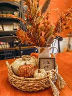 a basket filled with pumpkins and leaves on top of a wooden table next to a sign that says hello fall