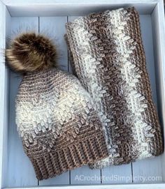 a knitted hat and scarf in a white box with a brown pom - pom