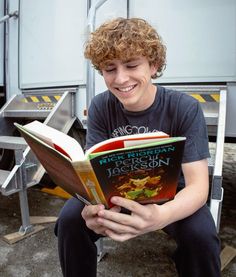 a young man reading a book while sitting on the ground in front of a truck