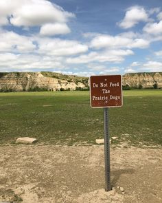 a do not feed the prairie dogs sign in front of a grassy field and cliff