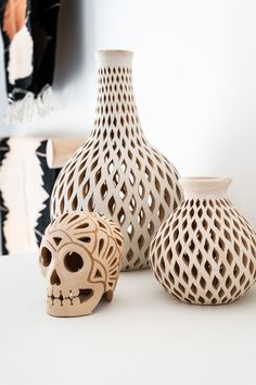 three ceramic vases sitting on top of a white table next to a skull head