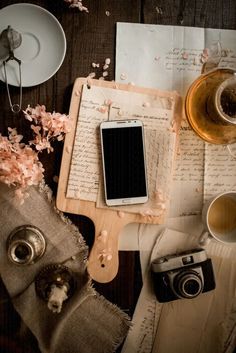 an old book, camera, and cup of tea on a wooden table with papers