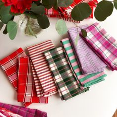 several plaid napkins are laid out on a table next to a vase with red flowers