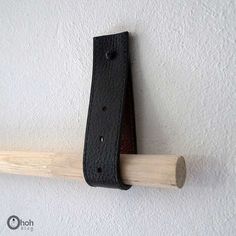 a black leather belt hanging on a white wall with a wooden stick in the foreground